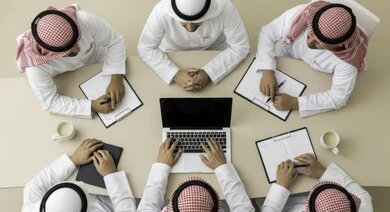 Overhead view of a business meeting between Saudi and Gulf Arab employees in a conference room. Understanding and cooperation between colleagues to achieve company goals. Comfortable work environment in Saudi companies. Use of modern technical devices in offices.