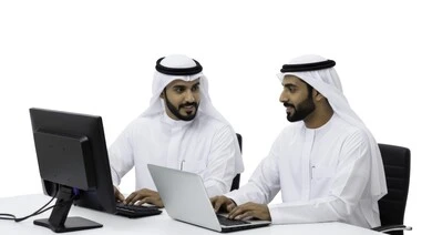  التفاهم والتعاون بين الزملاء لتحقيق أهداف الشركة , إدارة شؤون الأعمال وتنظيمها عبر الاجهزة التقنية، مهن ووظائف ادارية مكتبية، دمج العمل مع التقنية والتكنولوجيا، رجلان عربيان خليجيان اماراتيان يرتديان الكندورة والغتره يقومان بالعمل على الحاسوب داخل المكتب