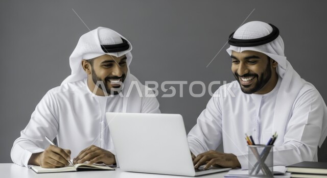  التفاهم والتعاون بين الزملاء لتحقيق أهداف الشركة , إدارة شؤون الأعمال وتنظيمها عبر الاجهزة التقنية، مهن ووظائف ادارية مكتبية، دمج العمل مع التقنية والتكنولوجيا، رجلان عربيان خليجيان اماراتيان يرتديان الكندورة والغتره يقومان بالعمل على الحاسوب داخل المكتب