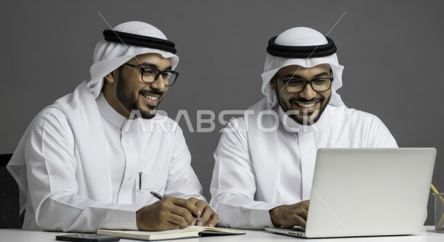 Writing reports and documents, understanding and cooperation between colleagues to achieve the company's goals, managing and organizing business affairs using modern technical equipment, two Emirati Gulf Arab men wearing kandura, ghutra and eyeglasses working on the laptop inside the office