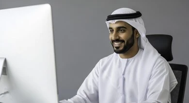 ادارة مهام العمل اليومية في مقر الشركة، مهن ووظائف اماراتية، استخدام الاجهزة التقنية الحديثة، رجل عربي خليجي اماراتي يرتدي الكندورة والغترة يجلس في مكتبه يعمل على الحاسوب بإيماءات السرور، تطوير خطط وآليه العمل, دمج العمل مع التقنية والتكنولوجيا