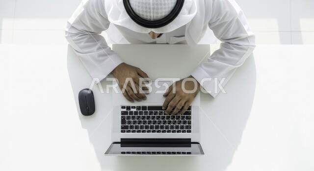 ادارة مهام العمل اليومية في مقر الشركة، مهن ووظائف اماراتية، استخدام الاجهزة التقنية الحديثة، صورة علوية لرجل عربي خليجي اماراتي يرتدي الكندورة والغترة يجلس في مكتبه يعمل على الحاسوب، تطوير خطط وآليه العمل, دمج العمل مع التقنية والتكنولوجيا