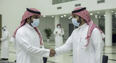 ارتداء الكمامة الطبية للوقاية من فايروس كورونا، اتخاذ الاجراءات الوقائية والاحترازية، صداقات وتعارف وبناء علاقات اجتماعية، الشراكة في الأعمال والمشاريع، رجلان عربيان خليجيان سعوديان يرتديان الثوب والشماغ يقومان بمصافحة بعضهما، توسيع مجالات العمل