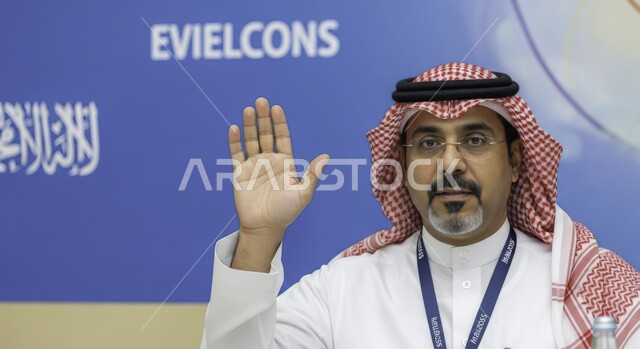 حركة يد وإشارات مختلفة, التحية والسلام والترحيب بشخص ما، رجل عربي خليجي سعودي يرتدي الثوب والشماغ والنظارة الطبية ويرفع يده بإيماءات طلب المشاركة في أمر ما، طلب الاذن للحديث في إحدى المؤتمرات