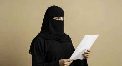 انجاز المهام المطلوبة, متابعة المراسلات والسجلات، امرأة عربية خليجية سعودية ترتدي النقاب والعباءة تحمل بيديها اوراق بيضاء، التدقيق في قراءة الملاحظات والتقارير، النظر إلى شيء ما، متابعة الخطط والتقارير