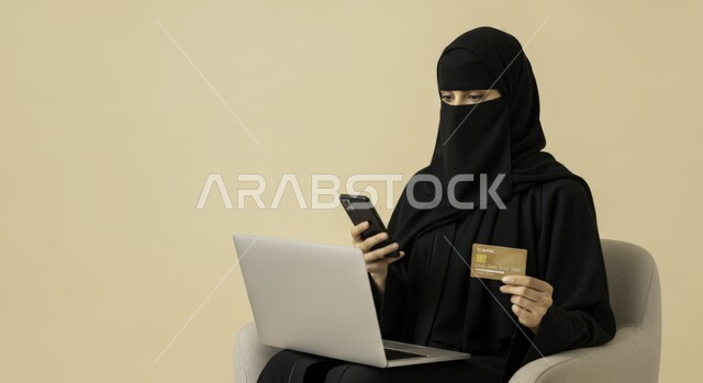 The ability to purchase and pay through electronic programs and applications, using modern technical devices for remote payment via the Internet, a veiled Saudi Arabian Gulf woman wearing an abaya sitting on a chair holding a phone, laptop, and bank credit card for online shopping