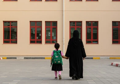 الشعور بالأمان والحب مع الآباء، موسم العودة للمدارس في السعودية، مفهوم الاعتناء بالأبناء والاهتمام بهم، بنت عربية خليجية سعودية ترتدي الزي المدرسي تضع الحقيبة على ظهرها وتمسك بيد والدتها للدخول إلى المدرسة، الاستعداد للعام الدراسي