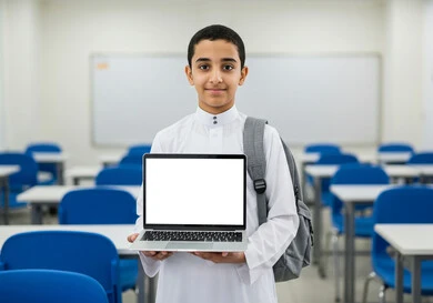 النظر غلى الكاميرا بإيماءات السعادة، دمج التكنولوجيا بالتعليم في المملكة العربية السعودية, عرض شاشة بيضاء فارغة، الاستعداد للعام الدراسي الجديد، طالب عربي خليجي سعودي يرتدي اليونيفوورم المدرسي وحقيبة الظهر المدرسية يحمل بيده حاسوب محمول، العودة إلى المدرسة