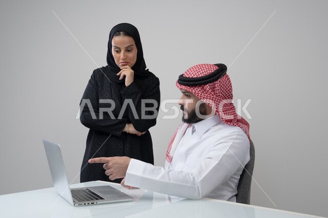 تبادل الخبرات والمعلومات لتحقيق الاهداف, الحوار و النقاش بين الزملاء، بيئة العمل المريحة في الشركات السعودية، بورتريه لموظفان عربيان خليجيان سعوديان يعملان في مكتبهم داخل مقر الشركة، استخدام الحاسب والتقنية في مجال الاعمال، خلفية رمادية