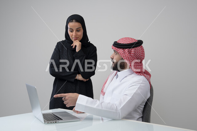 تبادل الخبرات والمعلومات لتحقيق الاهداف, الحوار و النقاش بين الزملاء، بيئة العمل المريحة في الشركات السعودية، بورتريه لموظفان عربيان خليجيان سعوديان يعملان في مكتبهم داخل مقر الشركة، استخدام الحاسب والتقنية في مجال الاعمال، خلفية رمادية