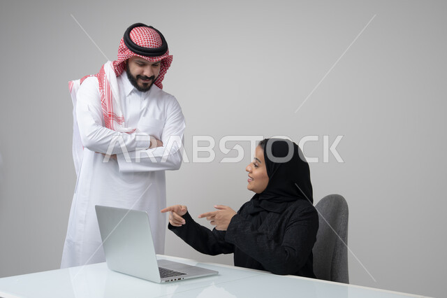 الحوار و النقاش بين الزملاء، بيئة العمل المريحة في الشركات السعودية، تبادل الخبرات والمعلومات لتحقيق الاهداف, بورتريه لموظفان عربيان خليجيان سعوديان يعملان في مكتبهم داخل مقر الشركة، استخدام الحاسب والتقنية في مجال الاعمال، خلفية رمادية