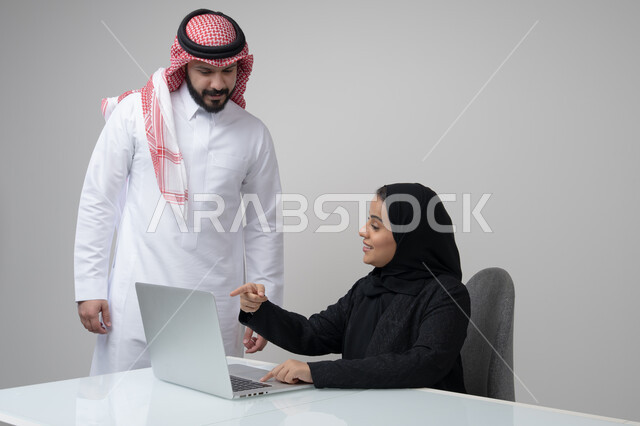 الحوار و النقاش بين الزملاء، بيئة العمل المريحة في الشركات السعودية، تبادل الخبرات والمعلومات لتحقيق الاهداف, بورتريه لموظفان عربيان خليجيان سعوديان يعملان في مكتبهم داخل مقر الشركة، استخدام الحاسب والتقنية في مجال الاعمال، خلفية رمادية