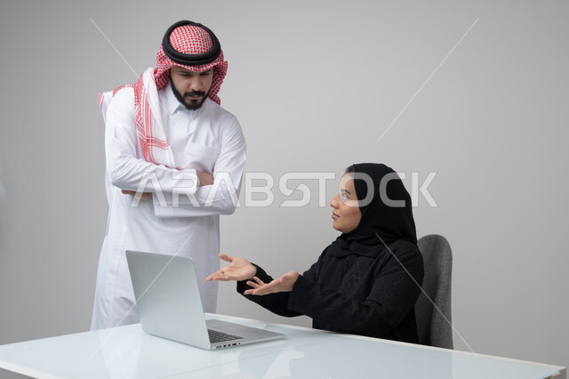 بيئة العمل المريحة في الشركات السعودية، الحوار و النقاش بين الزملاء، تبادل الخبرات والمعلومات لتحقيق الاهداف, بورتريه لموظفان عربيان خليجيان سعوديان يعملان في مكتبهم داخل مقر الشركة، استخدام الحاسب والتقنية في مجال الاعمال، خلفية رمادية