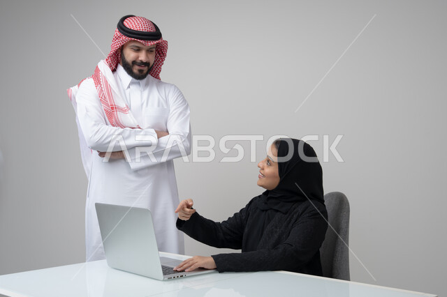 بيئة العمل المريحة في الشركات السعودية، الحوار و النقاش بين الزملاء، تبادل الخبرات والمعلومات لتحقيق الاهداف, بورتريه لموظفان عربيان خليجيان سعوديان يعملان في مكتبهم داخل مقر الشركة، استخدام الحاسب والتقنية في مجال الاعمال، خلفية رمادية