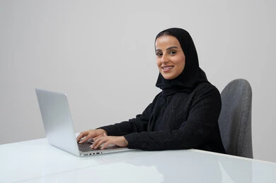 Office job and profession, managing and completing tasks using a modern and advanced technical device, portrait of a Saudi Arabian Gulf woman wearing a hijab and black abaya working on a laptop, gray background
