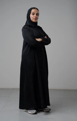 Looking at the camera with gestures of pleasure and self-confidence, the concept of elegance and interest in external appearance, portrait of a Saudi Arabian Gulf woman wearing the hijab and traditional abaya standing with crossed hands, full-length body image, gray background