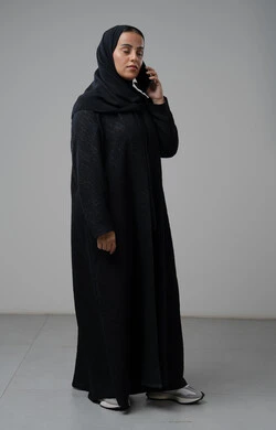 قضاء اوقات ممتعة بتبادل الاخبار والأحاديث، التحدث عبر الهاتف المحمول، بورتريه لامرأة عربية خليجية سعودية محجبة ترتدي العباءة تقوم بإجرء مكالمة هاتفية، محادثات ودردشات مع الاصدقاء، صورة الجسم بالكامل، خلفية رمادية