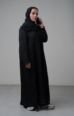 Having a good time exchanging news and conversations, talking on mobile phone, portrait of a veiled Saudi Arabian Gulf woman wearing an abaya making a phone call, conversations and chats with friends, full body image, gray background