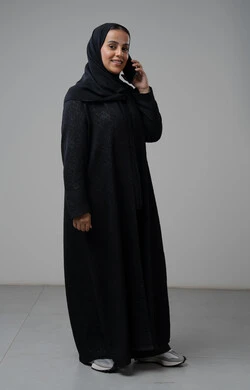 قضاء اوقات ممتعة بتبادل الاخبار والأحاديث، التحدث عبر الهاتف المحمول، بورتريه لامرأة عربية خليجية سعودية محجبة ترتدي العباءة تقوم بإجرء مكالمة هاتفية، محادثات ودردشات مع الاصدقاء، صورة الجسم بالكامل، خلفية رمادية