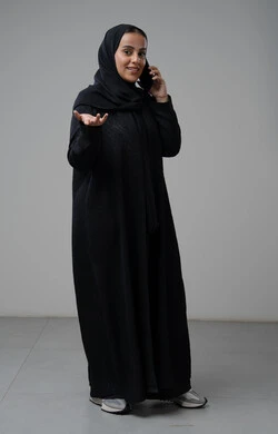 تبادل الاخبار والأحاديث عبر الجوال، التحدث عبر الهاتف المحمول، بورتريه لامرأة عربية خليجية سعودية محجبة ترتدي العباءة ترفع يدها بايماءات التساؤل وتقوم بإجرء مكالمة هاتفية، محادثة ودردشة مع الاصدقاء، صورة الجسم بالكامل، خلفية رمادية