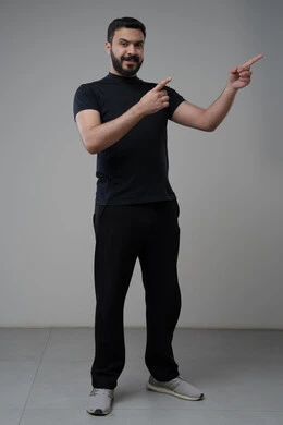 الإشارة إلى شيء ما, الوقوف باستقامة واعتدال, بورتريه لرجل عربي خليجي سعودي يرتدي الزي الكاجوال يشير باصبعي السبابة لمكان معين, صورة للجسم بالطول الكامل, خلفية رمادية
