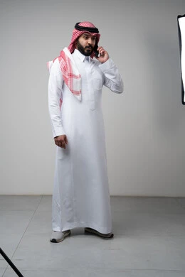 Chatting and conversation using a modern technical device, answering a phone call, portrait of a Saudi Arabian Gulf man wearing traditional thobe making a phone call through a mobile phone, full body image, white background