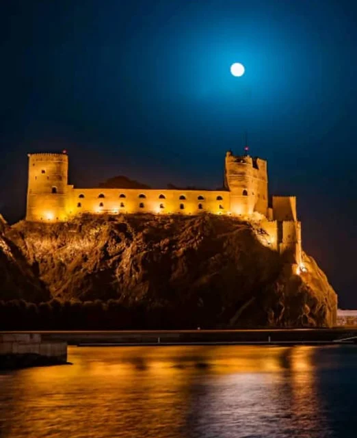 معلم وحصن عسكري تاريخي، موقع استراتيجي مهم مطل على خليج عمان, قلعة الميراني المبنية من الطين في سلطنة عمان المضاءة في وقت الليل ,التصميم والفن الهندسي المعماري على الطراز القديم، معلم ومزار سياحي تراثي مشهور في مدينة مسقط القديمة.