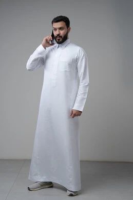 المحادثة والدردشة باستخدام جهاز تقني حديث, الرد على مكالمة هاتفية، بورتريه لرجل عربي خليجي سعودي يرتدي الثوب التقليدي يقوم باجراء اتصال هاتفي من خلال الهاتف المحمول، صورة الجسم بالطول الكامل, خلفية بيضاء