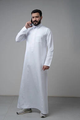 Conversation and chat using a modern technical device, answering a phone call, portrait of a Saudi Arabian Gulf man wearing traditional thobe making a phone call via mobile phone, full body image, white background