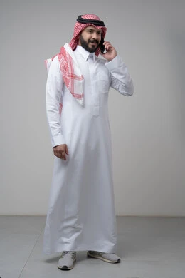 Chatting and conversation using a modern technical device, answering a phone call, portrait of a Saudi Arabian Gulf man wearing traditional thobe making a phone call through a mobile phone, full body image, white background