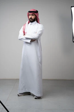 Taking selfies for official documents, taking care and attention to one's appearance, the concept of elegance and masculinity, a portrait of a young Saudi Arabian Gulf man wearing traditional clothing, standing with his hands crossed, looking at the camera with an expression of pleasure and self-confidence, full body, white background