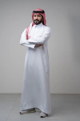  التقاط صور شخصية للوثائق الرسمية، الاعتناء والاهتمام بالمظهر الخارجي، مفهوم الاناقة والرجولة، بورتريه لشاب عربي خليجي سعودي يرتدي الثوب التقليدي يقف بأيدي متقاطعة ينظر الى الكاميرا بتعابير السرور والثقة بالنفس، الجسم بالطول الكامل، خلفية بيضاء