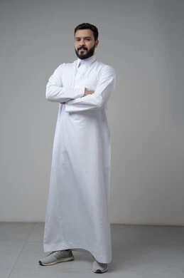  الاعتناء والاهتمام بالمظهر الخارجي، التقاط صور شخصية للوثائق الرسمية، مفهوم الاناقة والرجولة، بورتريه لشاب عربي خليجي سعودي يرتدي الثوب التقليدي يقف بأيدي متقاطعة ينظر الى الكاميرا بتعابير السرور والثقة بالنفس، الجسم بالطول الكامل، خلفية بيضاء