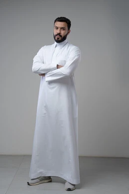  الاعتناء والاهتمام بالمظهر الخارجي، التقاط صور شخصية للوثائق الرسمية، مفهوم الاناقة والرجولة، بورتريه لشاب عربي خليجي سعودي يرتدي الثوب التقليدي يقف بأيدي متقاطعة ينظر الى الكاميرا بتعابير السرور والثقة بالنفس، الجسم بالطول الكامل، خلفية بيضاء
