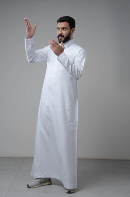 النظر الى الاعلى بتعابير التركيز، بورتريه لرجل عربي خليجي سعودي يرتدي الثوب التقليدي يشير بيده الى شيء ما، الدلالة على مكان معين، صورة الجسم بالطول الكامل، خلفية رمادية