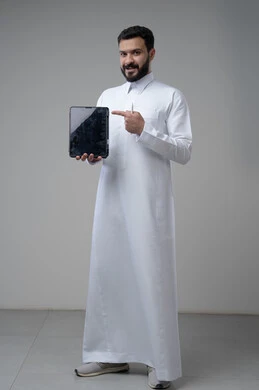 Blank black screen on tablet, browsing social media, using technology and modern technology, portrait of a Saudi Arabian Gulf man wearing traditional thobe holding a tablet and pointing at it with his index finger, full body image, gray background