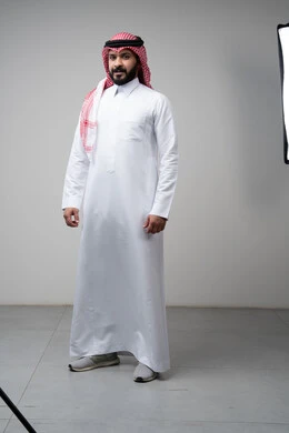 Taking care and attention to one's appearance, standing firmly and seriously, the concept of elegance and masculinity. Portrait of a Saudi Arabian Gulf man wearing a shemagh and traditional thobe, standing straight, looking at the camera with a confident expression, full body, gray background.