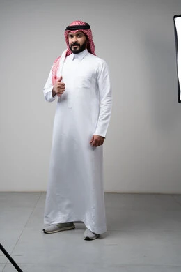 Using modern technology and techniques, browsing social media. Close-up portrait of a Saudi Arabian Gulf man wearing a traditional thobe and keffiyeh working on a tablet. Chatting with family and friends on the tablet with an expression of engagement. Gray background.  Thumbs up, looking at the camera with expressions of admiration and satisfaction. Portrait of a Saudi Arabian Gulf man wearing a keffiyeh and traditional thobe looking at the camera with gestures of acceptance and approval. Full-l