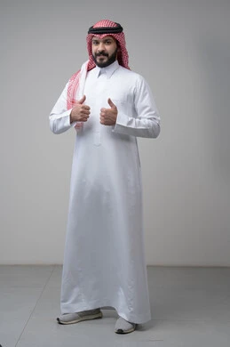 رفع اصابع الابهام الى الاعلى، النظر الى الكاميرا  بتعابير الاعجاب والرضا، بورتريه لرجل عربي خليجي سعودي يرتدي الشماغ والثوب التقليدي ينظر الى الكاميرا بايماءات القبول والموافقة، صورة الجسم بالطول الكامل، خلفية رمادية