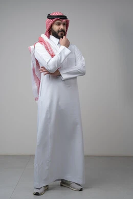 Looking forward and planning for the future, solving problems and making decisions, portrait of a Saudi Arabian Gulf man wearing a shemagh and a Saudi thobe, putting his hand on his chin with gestures of thinking and absent-mindedness, the concept of scrutiny and concentration, full-length body, gray background