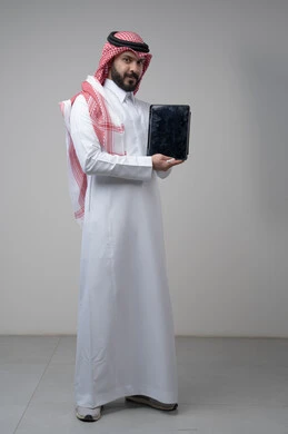 Blank black screen on tablet, browsing social media, using technology and modern technology, portrait of a Saudi Arabian Gulf man wearing a traditional shemagh and thobe holding a tablet in his hand looking at the camera with an expression of pleasure, full body image, gray background