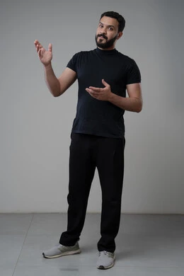 Looking up with an expression of concentration, portrait of a Saudi Arabian Gulf man in casual wear pointing at something, pointing to a specific place, full body image, gray background