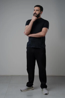 Looking forward and planning, problem solving and decision making, portrait of a Saudi Arabian Gulf man in casual wear putting his hand on his chin with gestures of thinking and absentmindedness, concept of scrutiny and concentration, full body, gray background