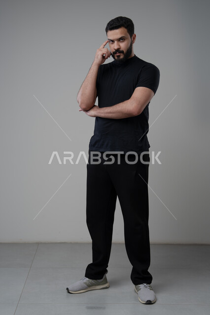 حل المشكلات واتخاذ القرارات، التطلع والتخطيط للمستقبل، بورتريه لرجل عربي سعودي خليجي يرتدي الزي الكاجوال يضع يده على رأسه بإيماءات التفكير وشرود الذهن، مفهوم التدقيق والتركيز، الجسم بالطول الكامل، خلفية رماديه