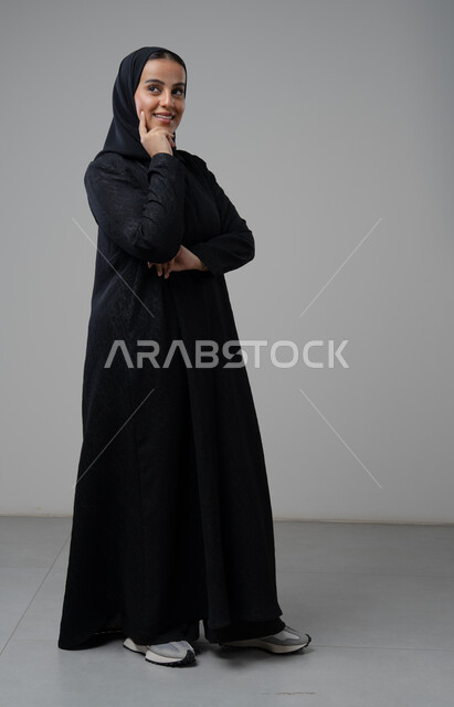 ايماءات التفكير والتمعن في أمر ما, بورتريه لامرأة عربية خليجية سعودية محجبة ترتدي العباءة السوداء تضع يدها على وجهها بإيماءات التأمل, صورة الجسم بالطول الكامل، خلفية بيضاء