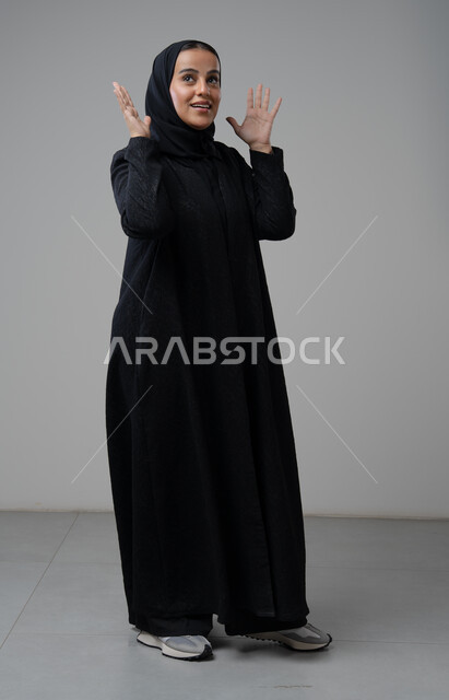 ايماءات الضجر والصداع, بورتريه لامرأة عربية خليجية سعودية محجبة ترتدي العباءة السوداء ترفع يديها بإيماءات التوتر والتعصيب, صورة الجسم بالطول الكامل، خلفية بيضاء