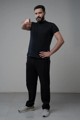 الاشارة إلى شيء ما بإيماءات السرور ,تعابير التأكد والتحديد,  بورتريه لرجل عربي خليجي سعودي مبتسم يرتدي الزي الكاجوال يرفع إصبعه السبابة للاختيار وينظر إلى الكاميرا بتعابير الجدية والحزم, صورة للجسم بالكامل, خلفية رمادية