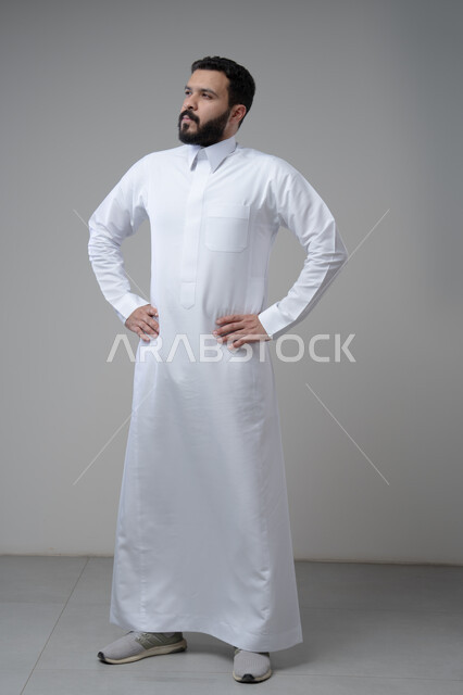 Taking care and attention to one's appearance, standing seriously and firmly, the concept of elegance and masculinity, a portrait of a young Saudi Arabian Gulf man wearing traditional clothing, standing straight, looking at the camera with an expression of self-confidence, full-length body, gray background