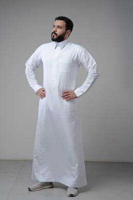 Taking care and attention to one's appearance, standing seriously and firmly, the concept of elegance and masculinity, a portrait of a young Saudi Arabian Gulf man wearing traditional clothing, standing straight, looking at the camera with an expression of self-confidence, full-length body, gray background