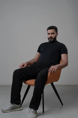  الاعتناء والاهتمام بالمظهر الخارجي، الجلوس بإيماءات الجدية والحزم، مفهوم الاناقة والرجولة، بورتريه لشاب عربي خليجي سعودي يرتدي الزي الكاجوال يجلس على كرسي وينظر الى الكاميرا بتعابير الثقة بالنفس، خلفية بيضاء